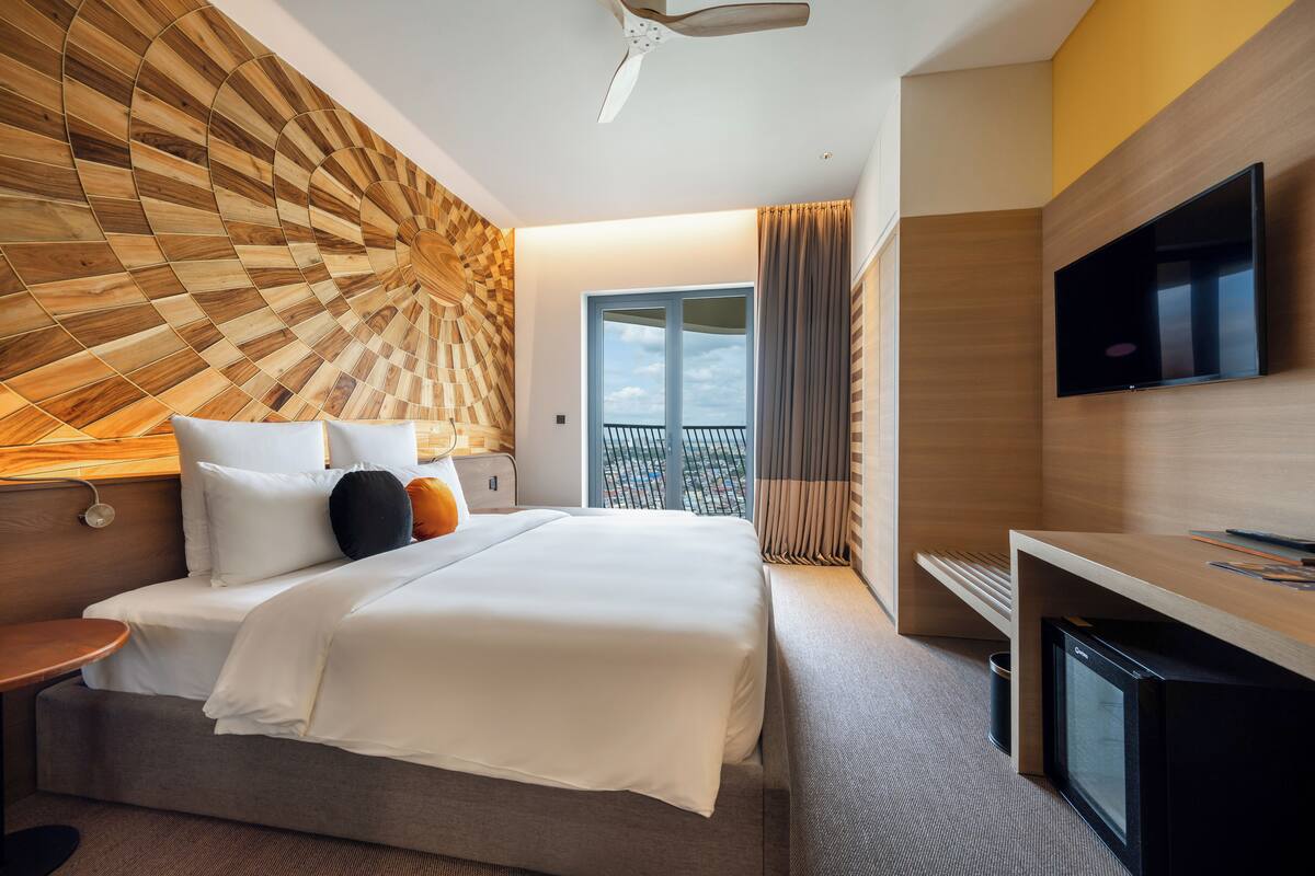 A modern hotel room with a bed, a desk, a television, and a view of the outdoors.