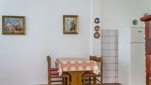 A dining area with a wooden table and chairs, a patterned tablecloth, and a white refrigerator in the background. - Simo A1, Punat (Punat)