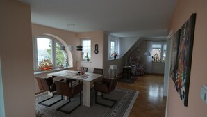 A dining area with a large table, chairs, and a view of the outdoors through a window.