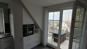 A modern kitchen with built-in appliances, a dining area with a view of the city, and a sliding glass door to the outdoors.