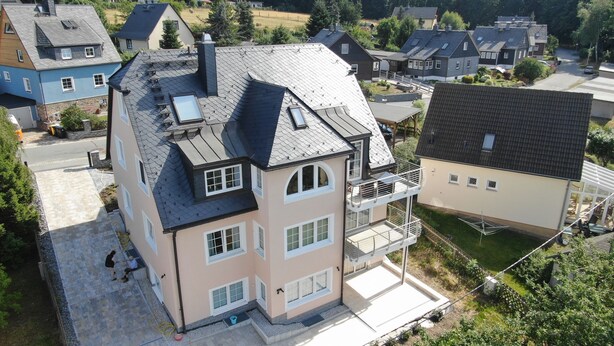 A multi-story house with a sloped roof, multiple windows, and a visible balcony.