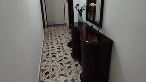 Un couloir doté d’un sol en terrazzo, d’une console en bois foncé agrémentée d’un miroir, et d’une porte au fond.