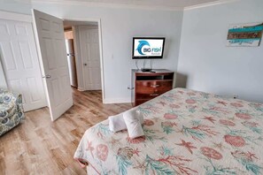 A hotel room with a bed, a TV on a stand, a wooden dresser, and a door leading to another room.