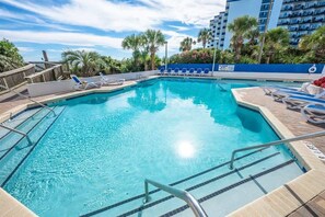 A clear blue pool with lounge chairs and a wooden deck.