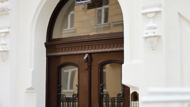 Puerta doble de madera con una reja de metal negro, pared blanca con molduras decorativas y un letrero sobre la puerta.