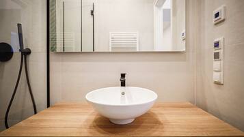 Un baño con tocador de madera, lavabo blanco, espejo y toallero.