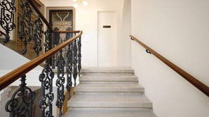 Una escalera con barandillas de metal negro ornamentado y una barandilla de madera, que conduce a una puerta con la inscripción 'MEZZANINE'.