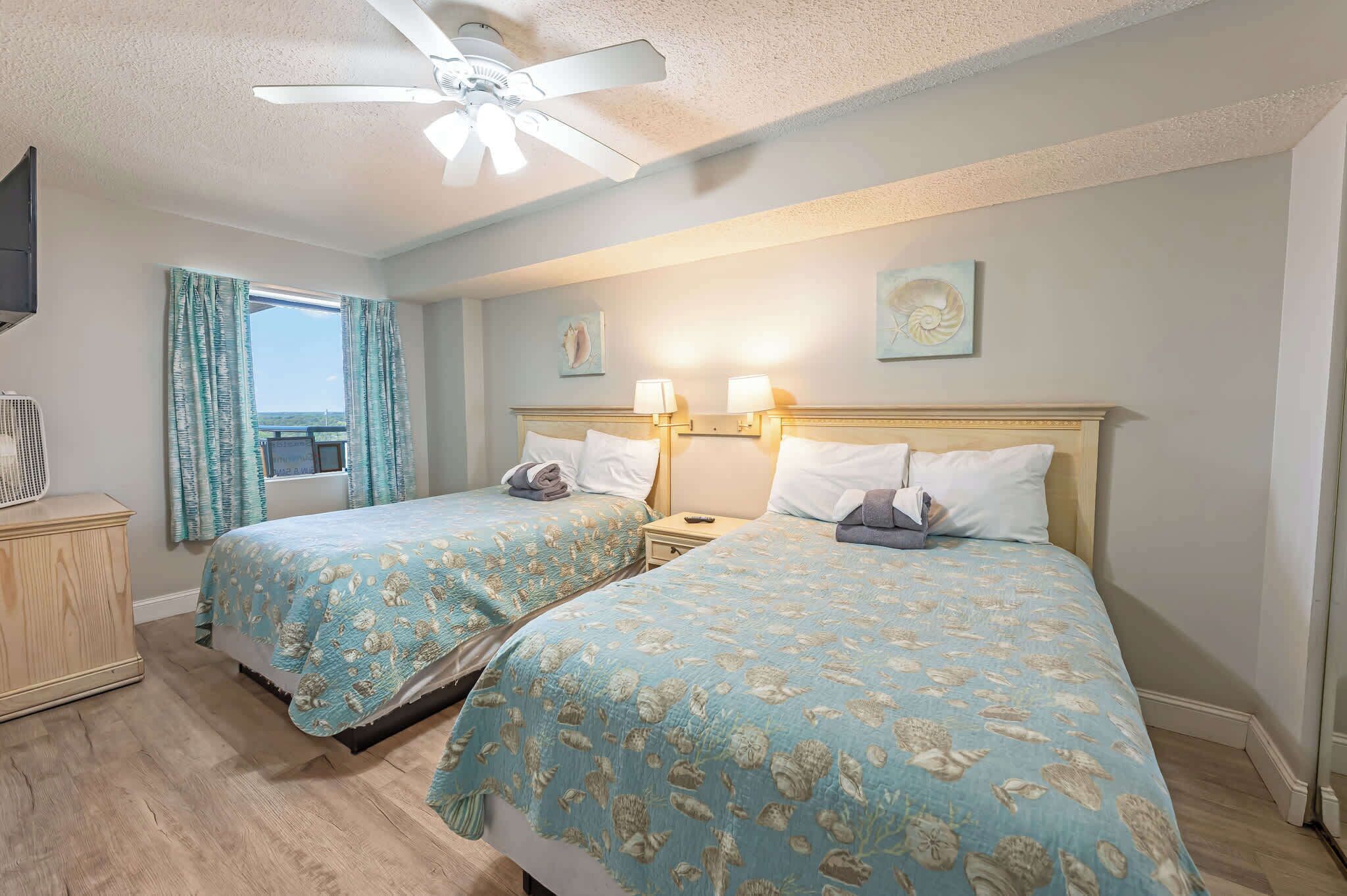 Ein Hotelzimmer mit zwei Betten, einem Deckenventilator, einem Vorhangfenster und Wandleuchten.