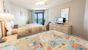 A hotel room with two beds, a TV, a ceiling fan, a balcony with a view, and a dresser.