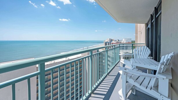A balcony with a view of the ocean, a white chair, and a railing.