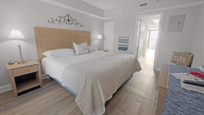 Une chambre à coucher comprenant un lit, des tables de chevet, une lampe, un élément de décoration murale et une vue sur le couloir.