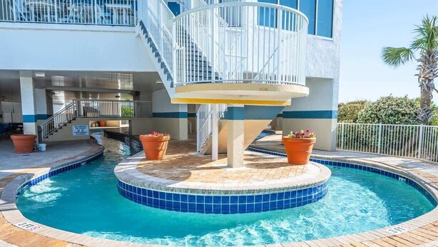 Une piscine de forme circulaire, entourée d’une terrasse carrelée et agrémentée de plantes en pot.