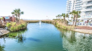 Un canal d’eau avec une fontaine, bordé de palmiers et d’un bâtiment portant l’inscription « TOUR SUD ».