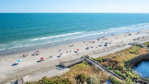 Une plage avec une promenade en bois qui mène à l’eau, une plage de sable et une vue dégagée sur l’océan.