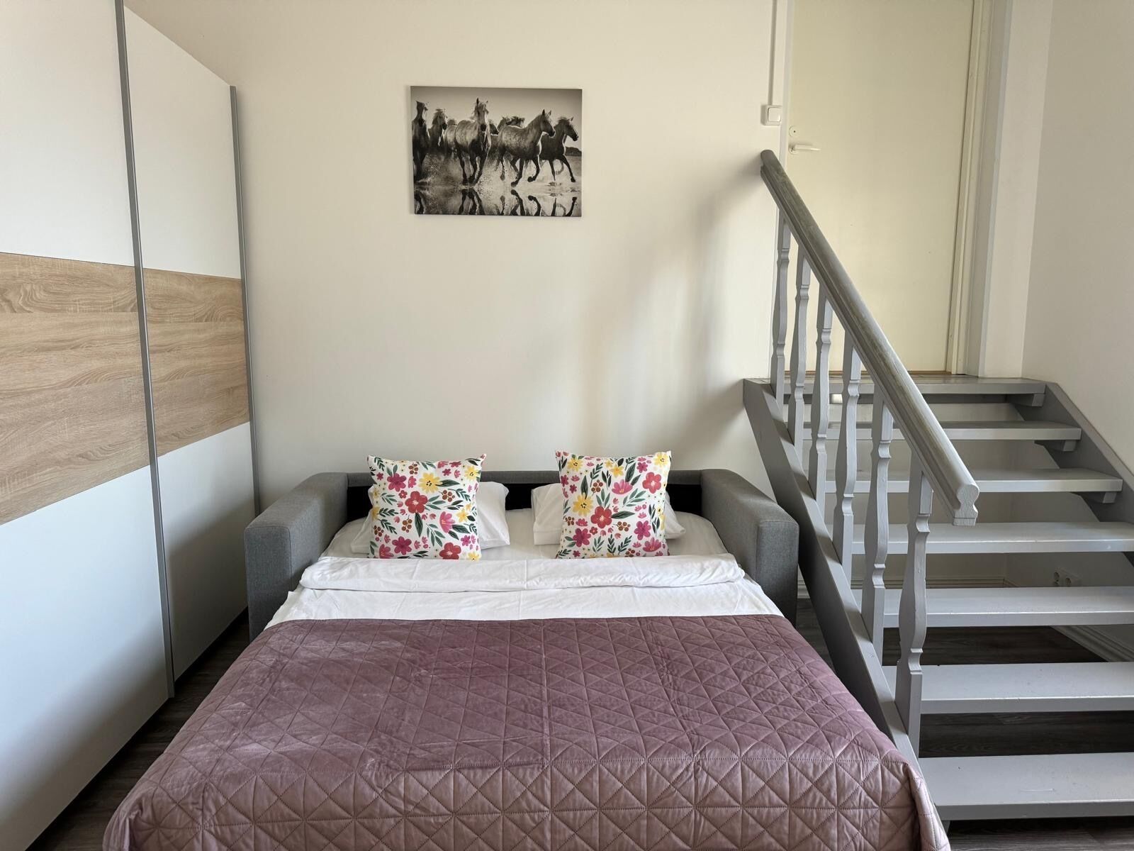 A bedroom with a bed, a staircase, and a wall-mounted picture.