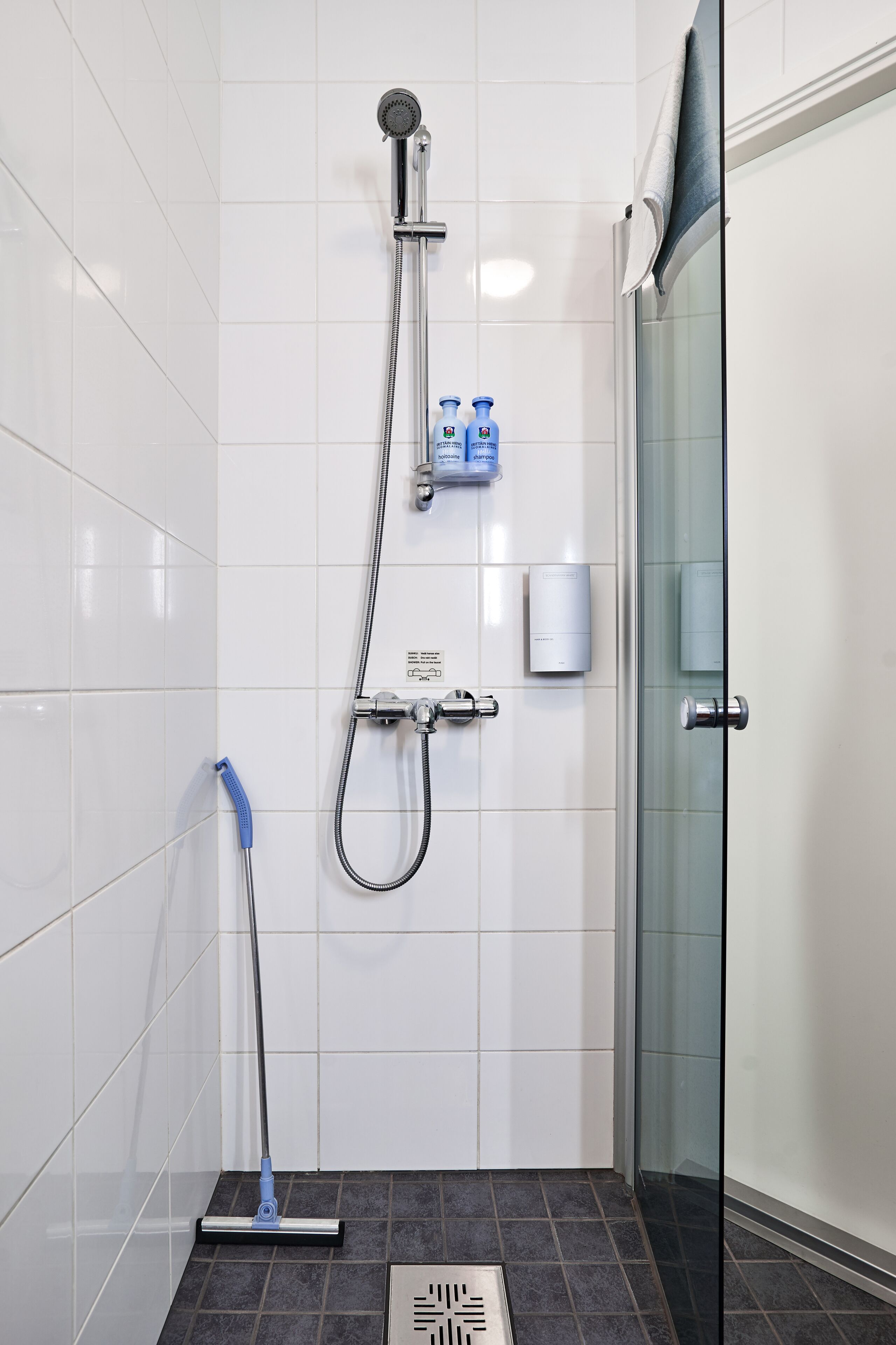 A modern bathroom with a shower, a handheld showerhead, a handheld shower brush, and a glass shower door.