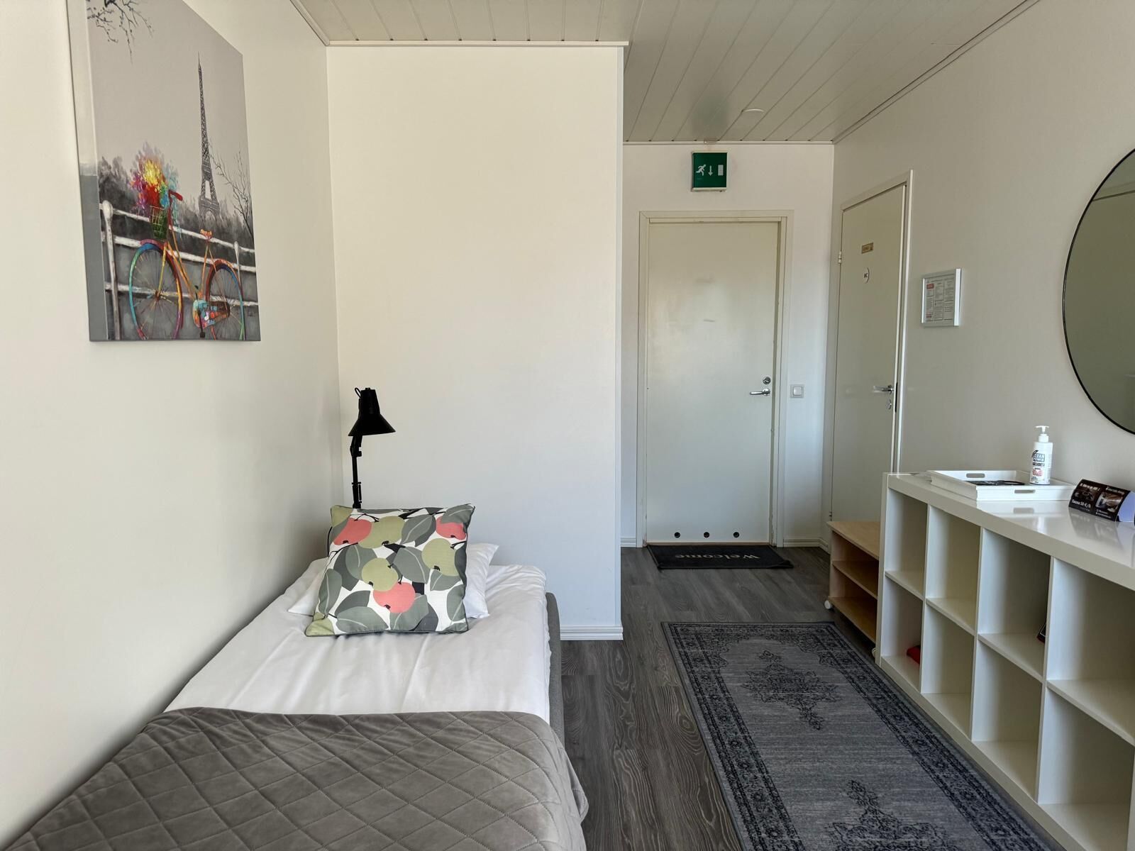 Habitación de hotel con cama, escritorio con espejo, alfombra pequeña y un cuadro de una bicicleta.