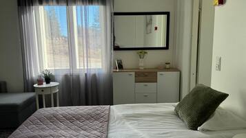 A bedroom with a bed, a bedside table, a dresser, a mirror, and a window with curtains.