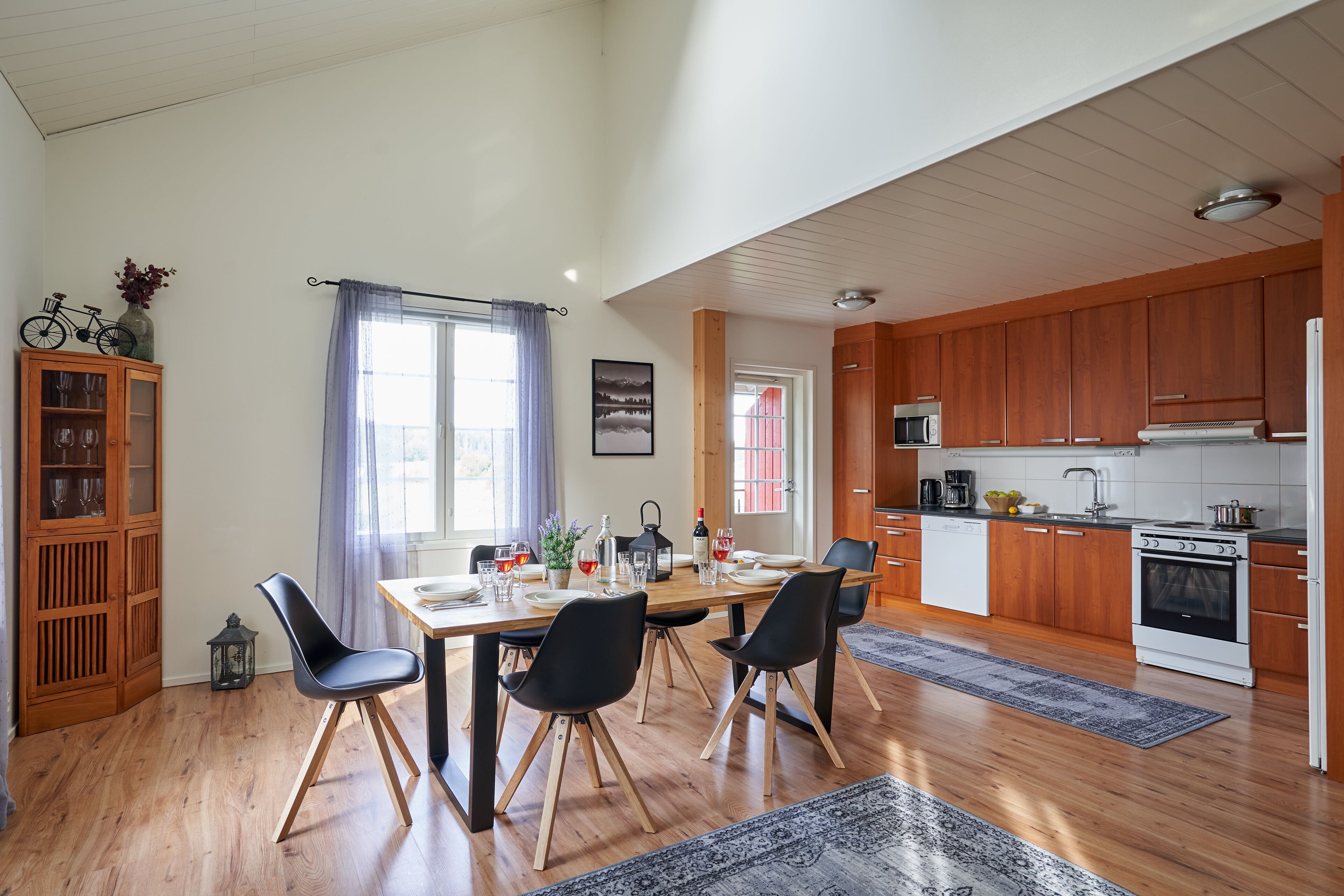 A modern kitchen with wooden cabinets, a white stove, and a dining area with a wooden table and black chairs.