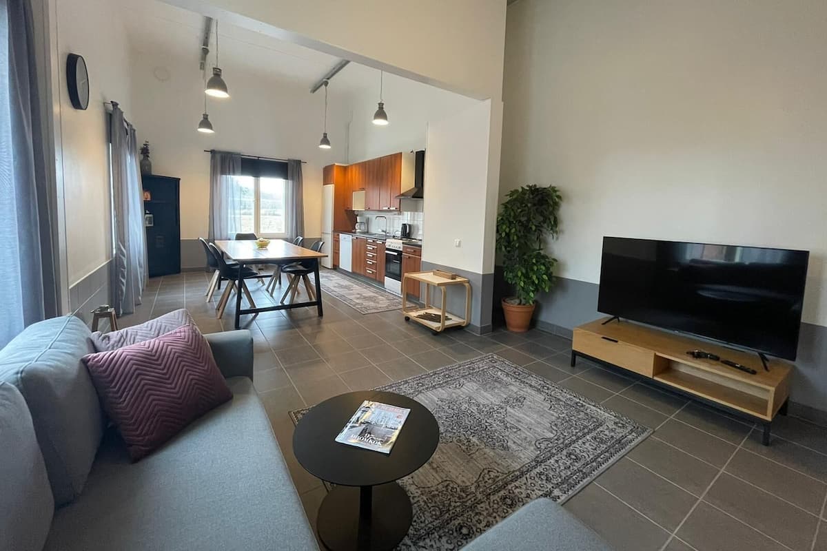 A modern living room with a sofa, a coffee table, a TV, and a kitchen in the background.
