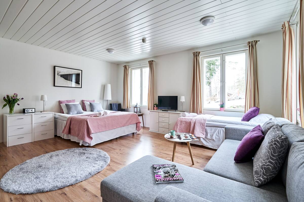 A modern bedroom with a bed, a sofa, a TV, and a window with curtains.