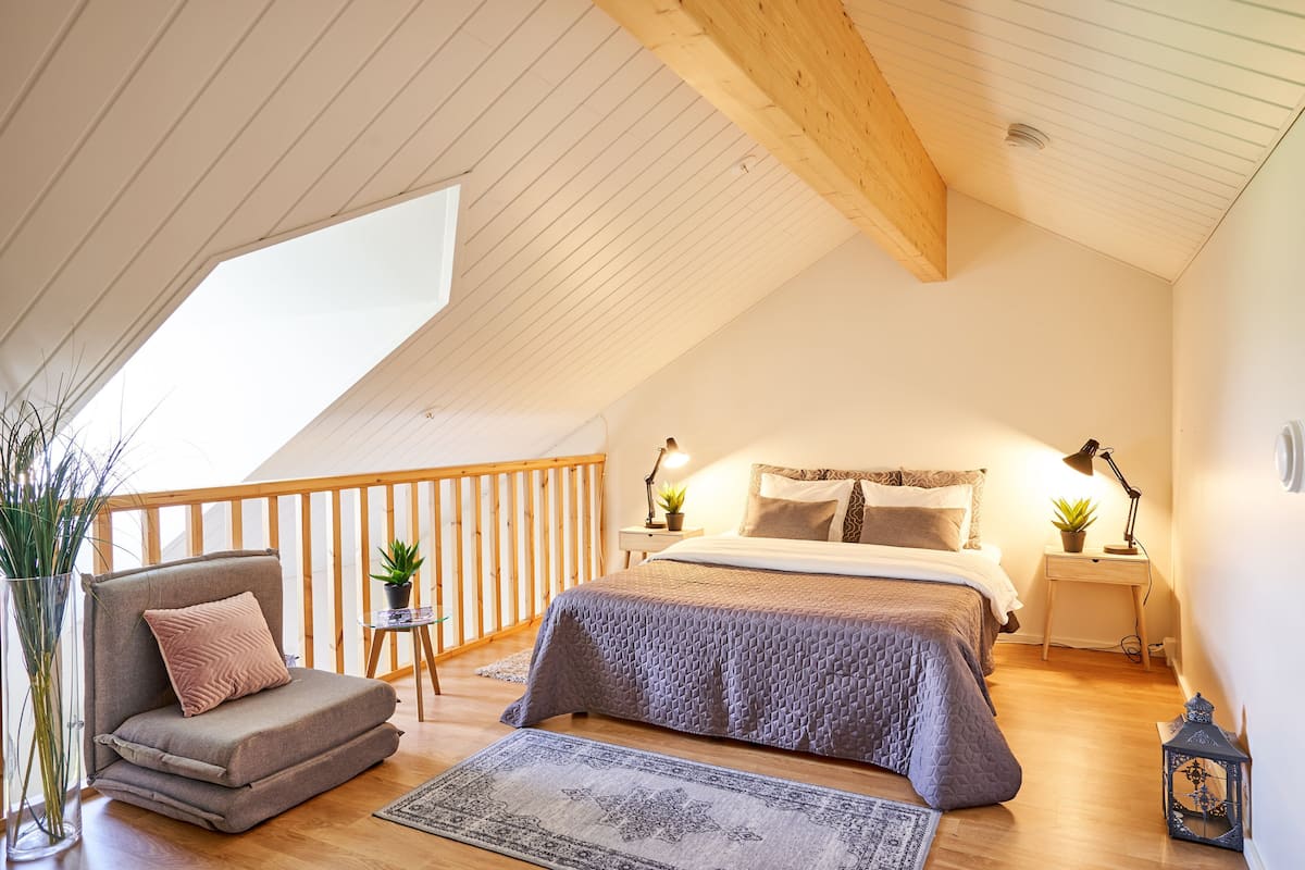 A cozy bedroom with a bed, bedside tables, a chair, and a small table with a plant.