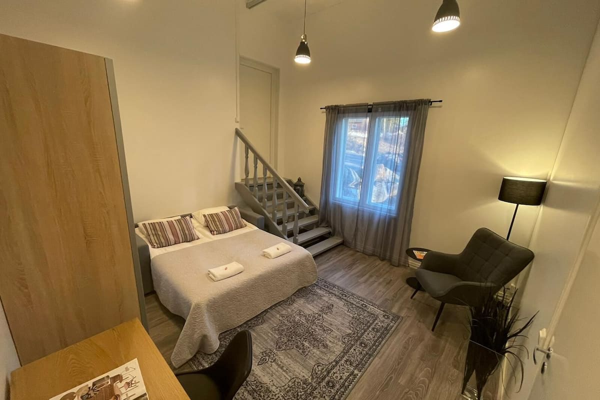 A bedroom with a bed, a chair, a rug, a staircase, and a lamp.