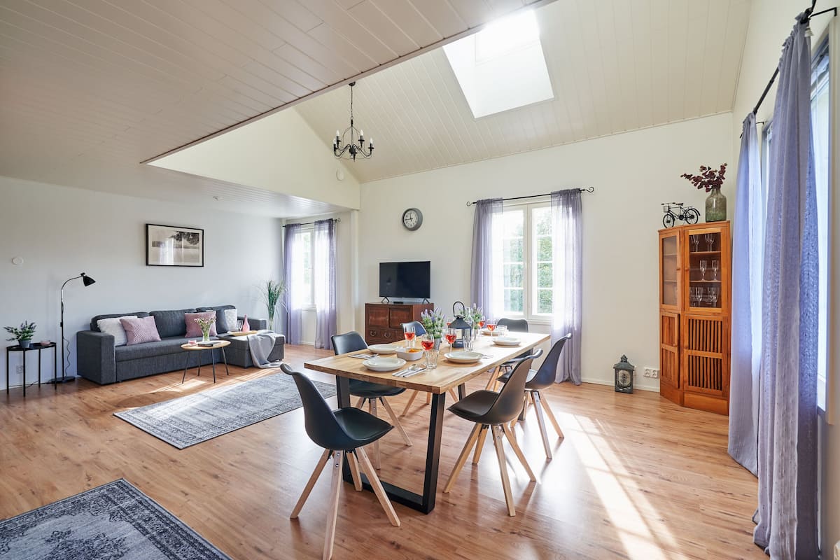 A spacious living room with a dining area, wooden flooring, a sofa, a TV, and a cabinet with glass doors.