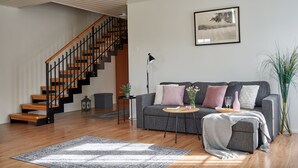 A modern living room with a staircase, a grey sofa with cushions, a small round table, and a potted plant. - Apartments in Porvoo (Porvoo)