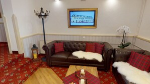 A cozy living room with a brown leather sofa, red and black plaid pillows, a wooden coffee table with a candle, and a framed picture on the wall. - "Landhaus Idylle" 1 apartment in Landhaus Gretl  (Krumpendorf am Wörthersee)