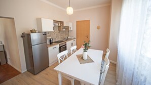 A compact kitchen with a refrigerator, oven, and sink. There is a dining table with chairs and a potted plant. - "Landhaus Idylle" 1 apartment in Landhaus Gretl  (Krumpendorf am Wörthersee)