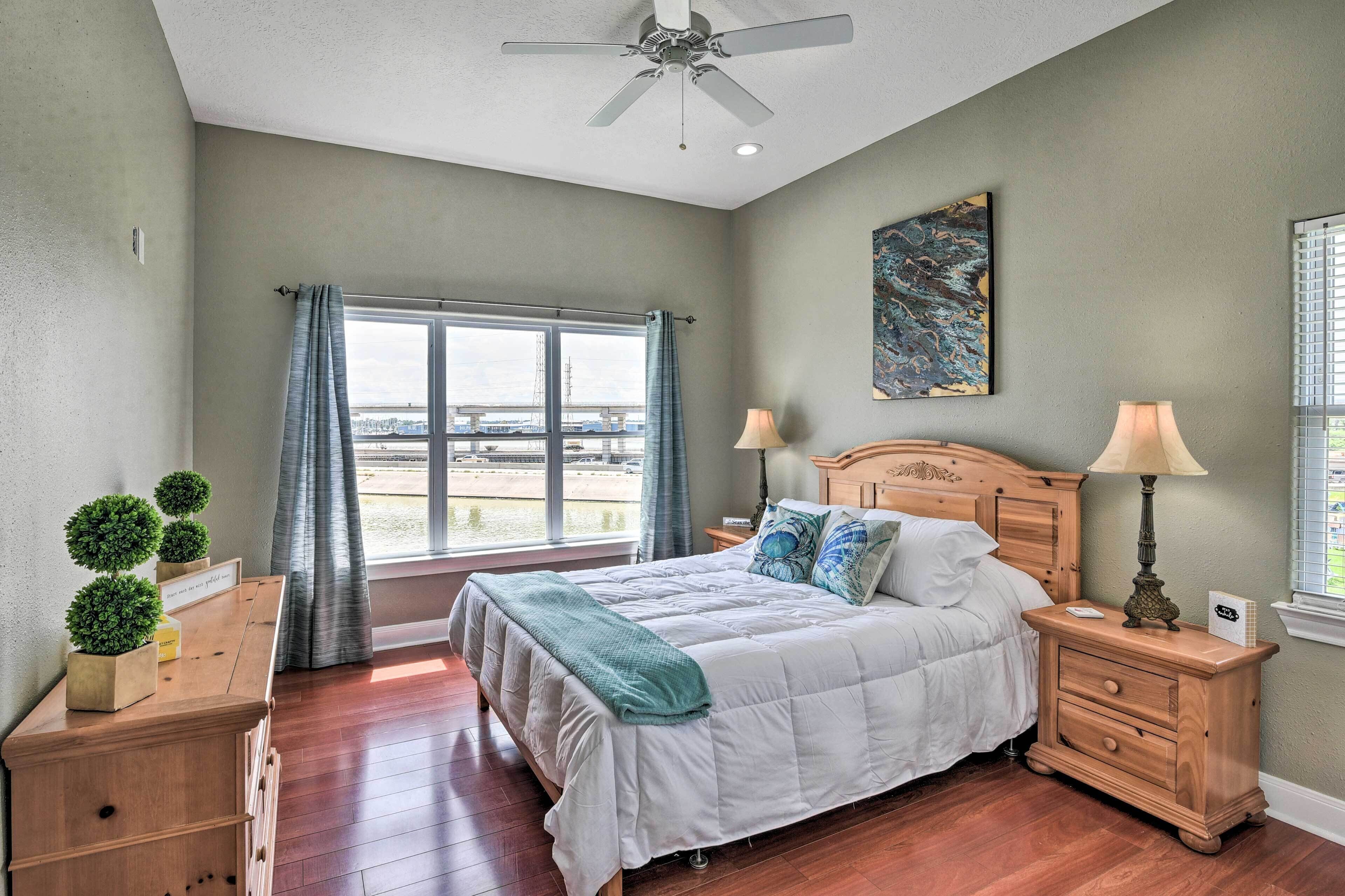 Quarto com cama, mesas de cabeceira, ventilador de teto, janela com cortinas e vista para o exterior.
