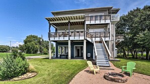Une maison à deux étages dotée d’un balcon, d’un foyer extérieur et de deux fauteuils Adirondack.