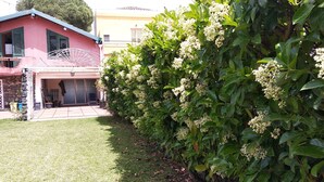 A house with a pink exterior, a covered porch, and a well-maintained garden with flowering shrubs. - Villa With Large Garden Close to the Sea, Between Etna and Taormina (Acireale)