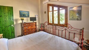 A bedroom with a wooden ceiling, a green door, a bed with a metal headboard, a dresser, a TV, and two framed pictures on the wall. - Villa With Large Garden Close to the Sea, Between Etna and Taormina (Acireale)