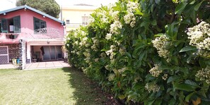 A house with a pink exterior, a covered porch, and a well-maintained garden with flowering shrubs. - House With Garden Near the sea (Acireale)