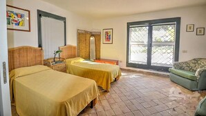 A room with two beds, a small table, a bench, a window with a view, and artwork on the walls.