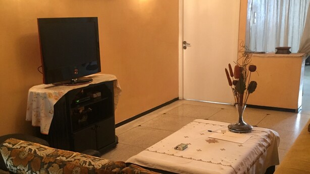 A living room with a sofa, a television on a stand, a door, and a window with curtains. - Room-property Located in a Quiet Area cl (Casablanca)