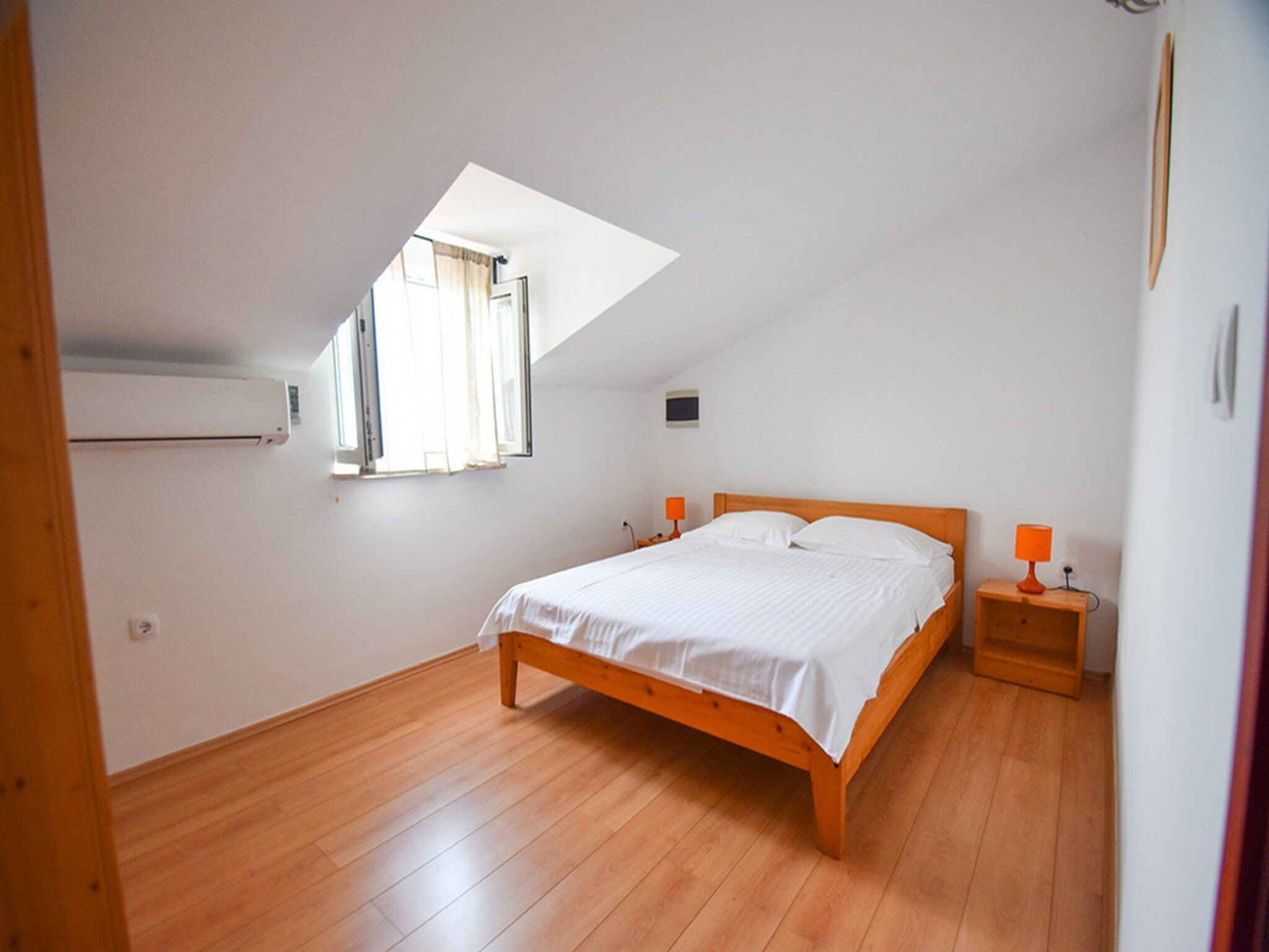 A bedroom with a sloped ceiling, a bed with white bedding, two bedside tables with lamps, and a window with curtains.