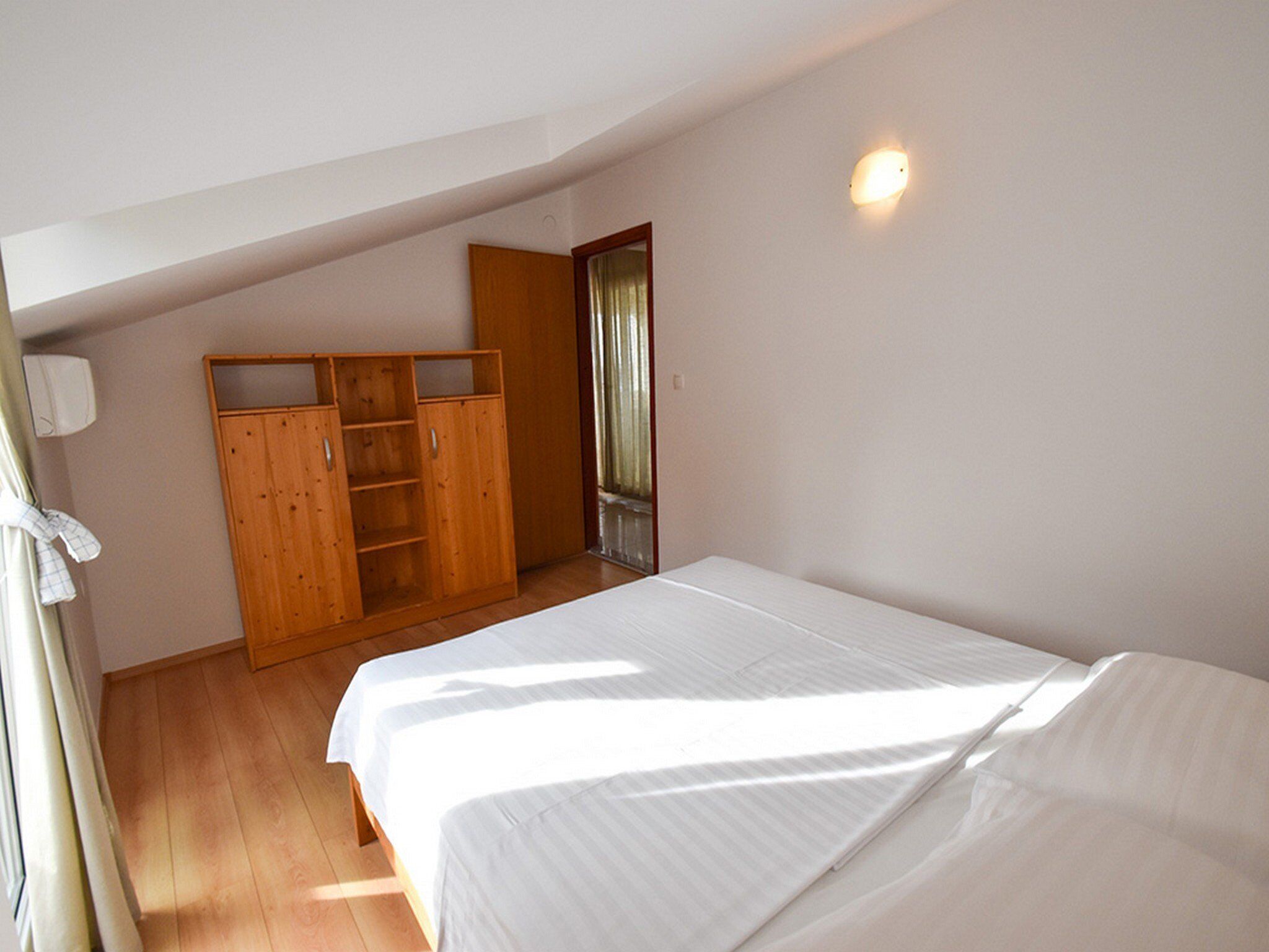 A bedroom with a single bed, wooden wardrobe, and a small window.