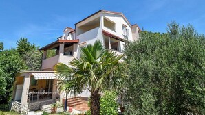 A multi-story building with a balcony, surrounded by greenery and trees. - Apartments Jaklin (Rab)