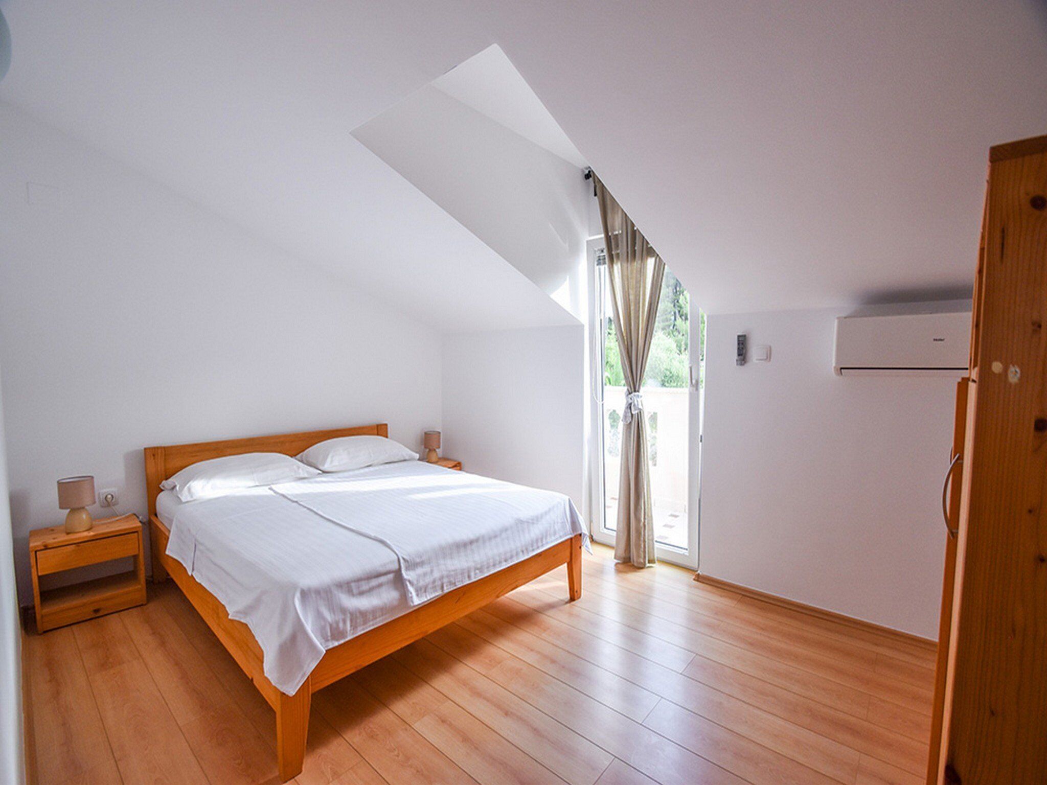 Une chambre à coucher avec un lit en bois, une table de chevet, une fenêtre avec des rideaux et un appareil de climatisation.