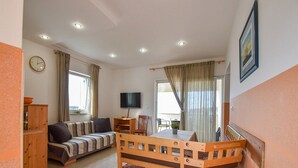 A spacious living area with a sofa, a wooden dining table with chairs, a television, and a clock on the wall. - Apartments Jaklin (Rab)
