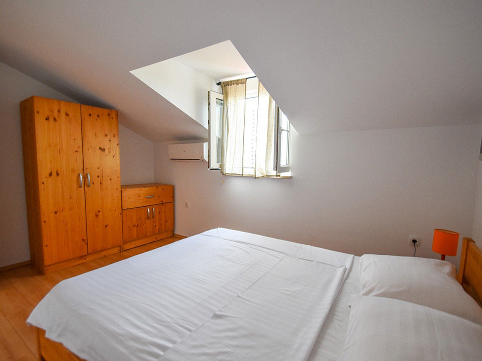 Un dormitorio con una cama grande, un armario de madera, una ventana con cortinas y un tragaluz.