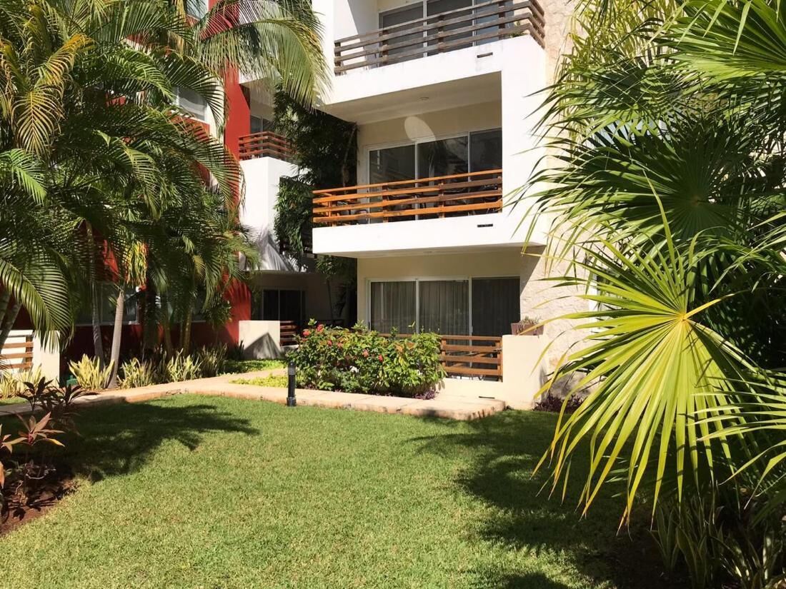 A modern building with balconies, a well-maintained lawn, and tropical plants.