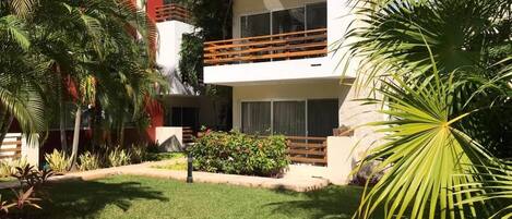 A modern building with balconies, a well-maintained lawn, and tropical plants.