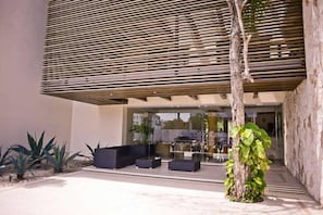 Un edifici modern amb un sostre de lamel·les, seients a l'exterior i un arbre.