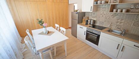 A compact kitchen with wooden cabinets, a white countertop, and a dining area with a table and chairs.