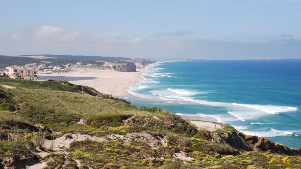 Un paisaje costero con una playa, acantilados y un pueblo a lo lejos.