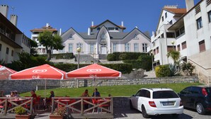 Un hotel con un patio central, zona de estar al aire libre con sombrillas rojas y un coche blanco estacionado al frente.